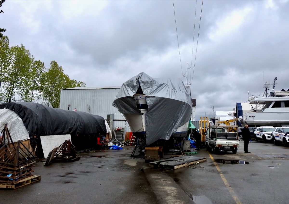 A large boat sitting on a paved parking lot. The boat is covered with a silver tarp.