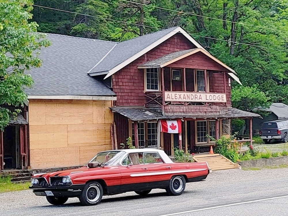 A car passes an aging red building with a sign announcing &lsquo;Alexandra Lodge.&rsquo; 