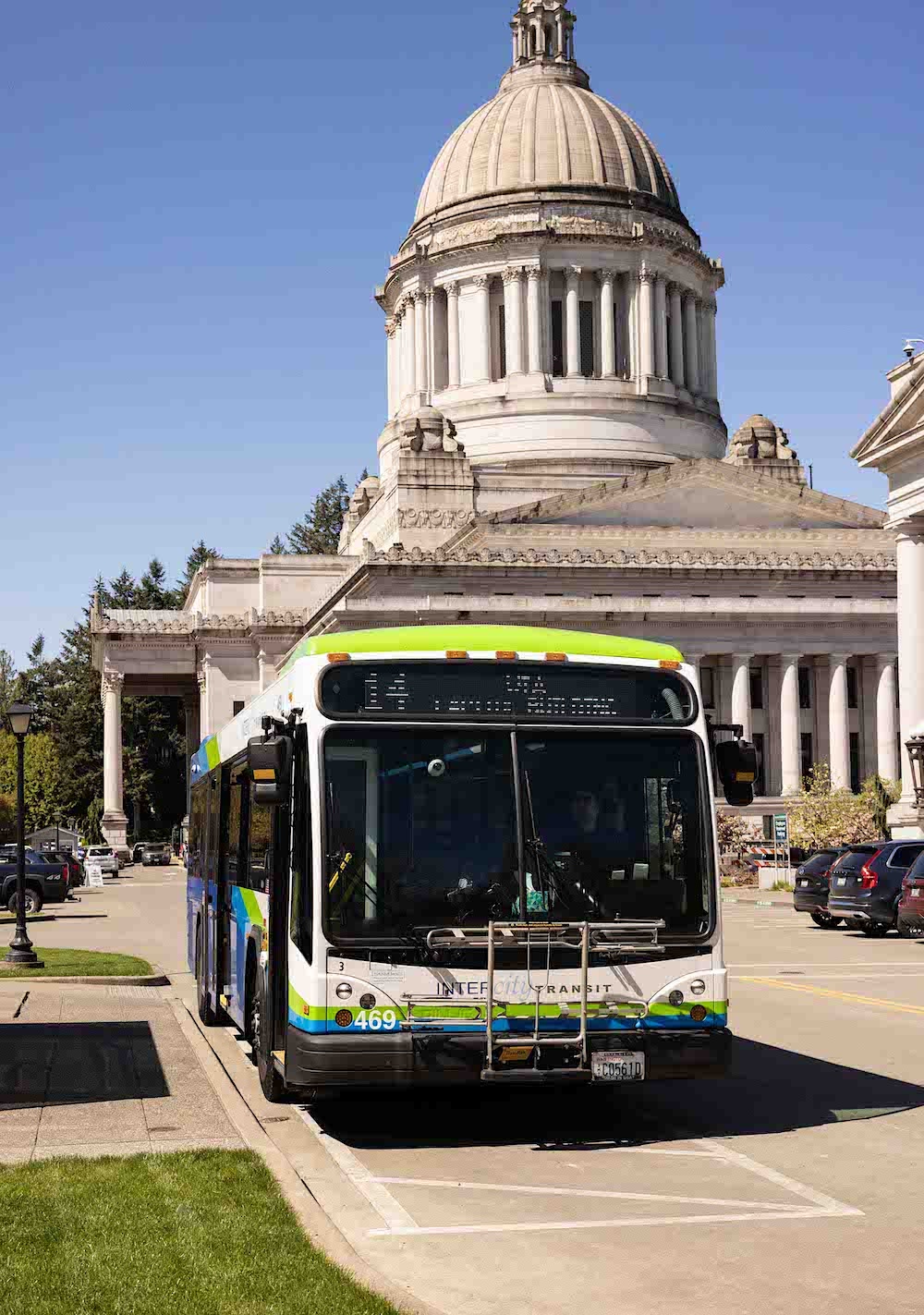 A white, blue and green Intercity Transit bus stops in front of the Washington state capitol building in Olympia. It is the No. 14 bus.
